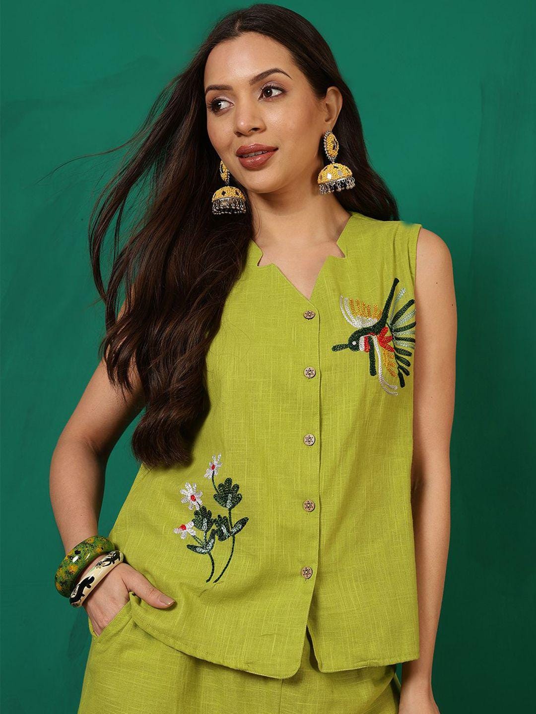 Puede incluir: Una blusa sin mangas de color verde lima con cuello en V y cierre de botones. La blusa presenta diseños bordados de flores y colibríes. La modelo lleva pendientes y pulseras doradas. El conjunto se combina con un pantalón corto a juego.