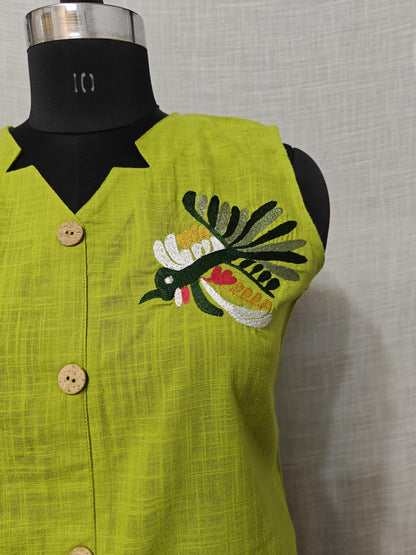 Puede incluir: Un chaleco sin mangas de color verde lima con cuello negro y botones de madera. El chaleco presenta un diseño de pájaro bordado en blanco, verde, amarillo y rojo. La tela tiene una apariencia texturizada.