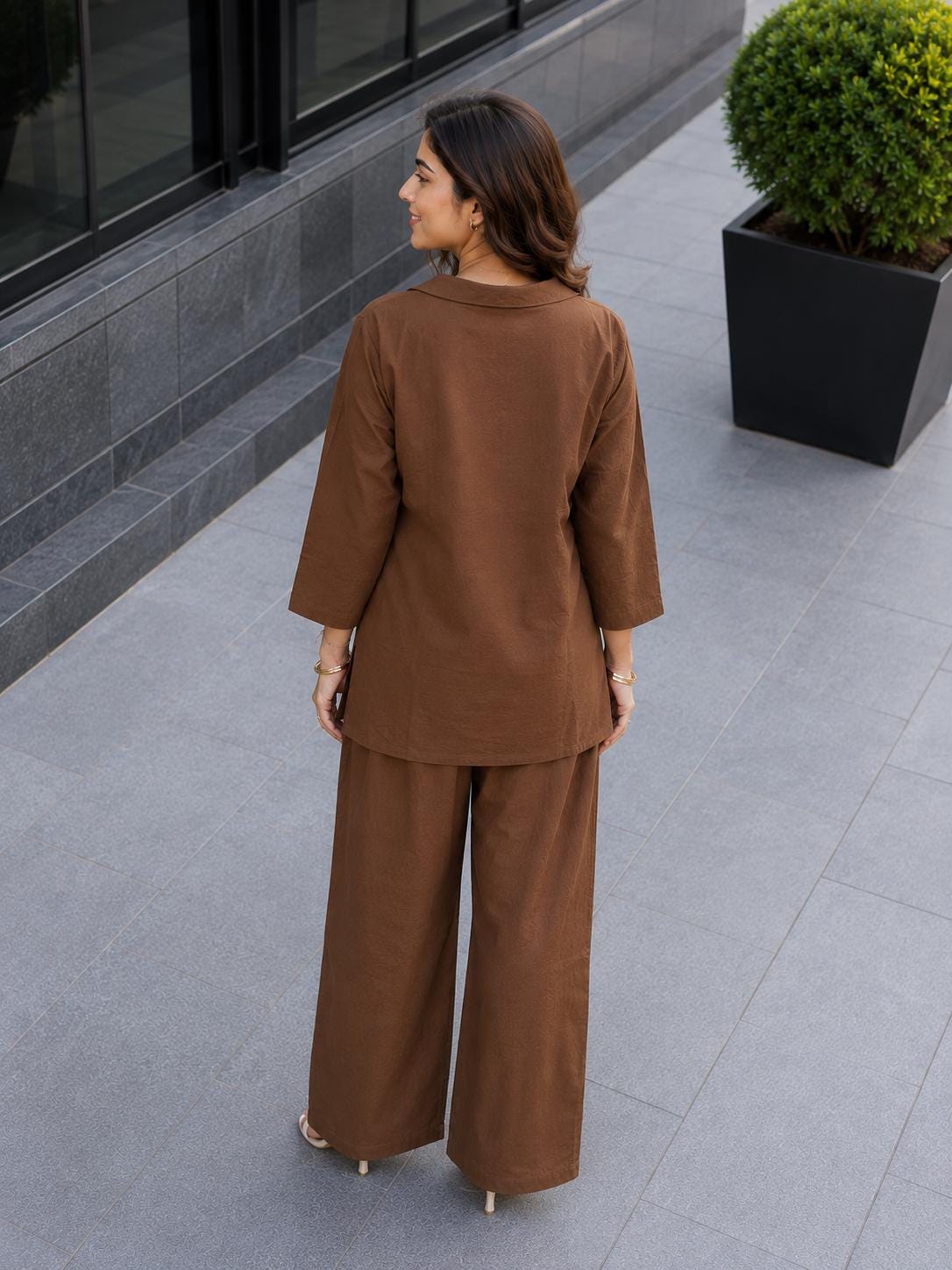 May include: A solid brown two-piece set consisting of a long-sleeved tunic top with a collared neckline and matching wide-leg trousers. The outfit features a consistent earthy brown tone throughout, with a relaxed fit and straight hemline on the top.