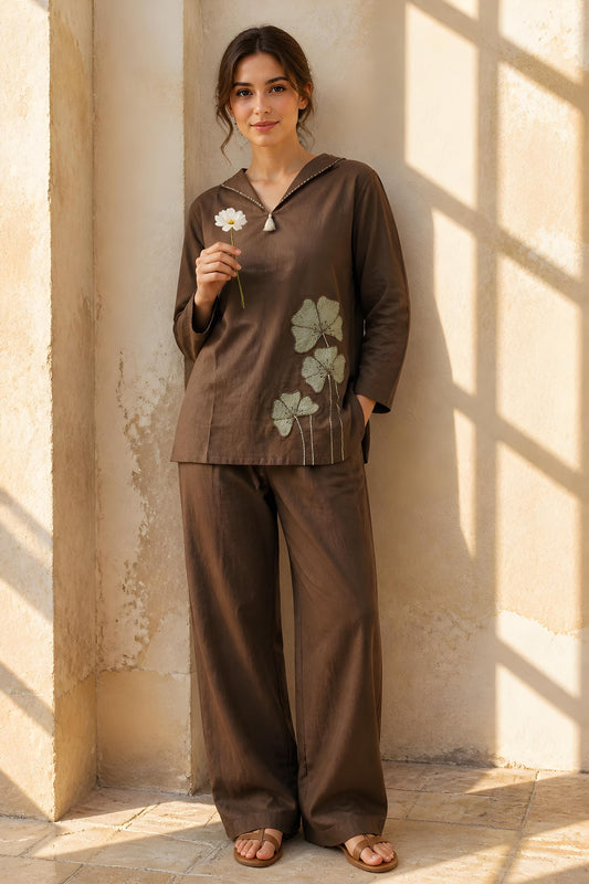 May include: A dark brown long-sleeved tunic top with a V-neckline and a small tassel detail, featuring light green floral embroidery on the lower left side, paired with matching dark brown wide-leg trousers and brown flat sandals.