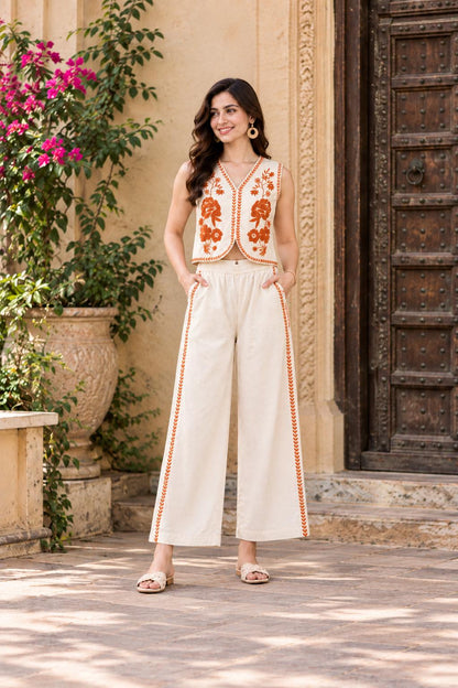 May include: A sleeveless cream-coloured vest featuring orange floral embroidery along the front edges, paired with matching wide-leg trousers that have a vertical orange embroidered stripe down each side and two side pockets.